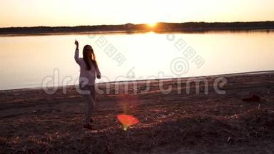 一个年轻的女人在春天的河滩上<strong>享受</strong>金色<strong>时光</strong>的日落
